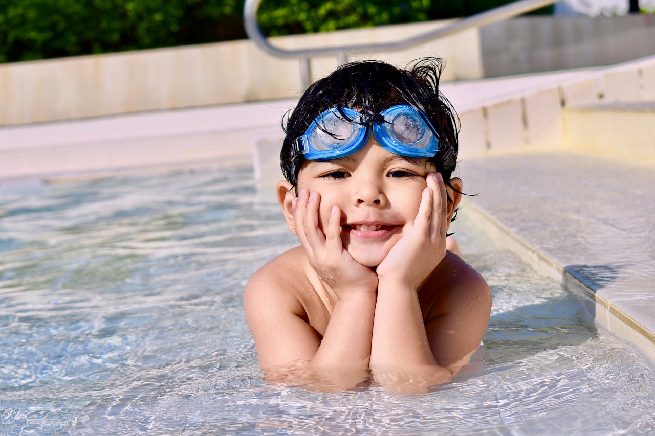 The Art of Drawing Readers In: Your attractive post title goes here A young child with goggles smiling while playing in an outdoor swimming pool.